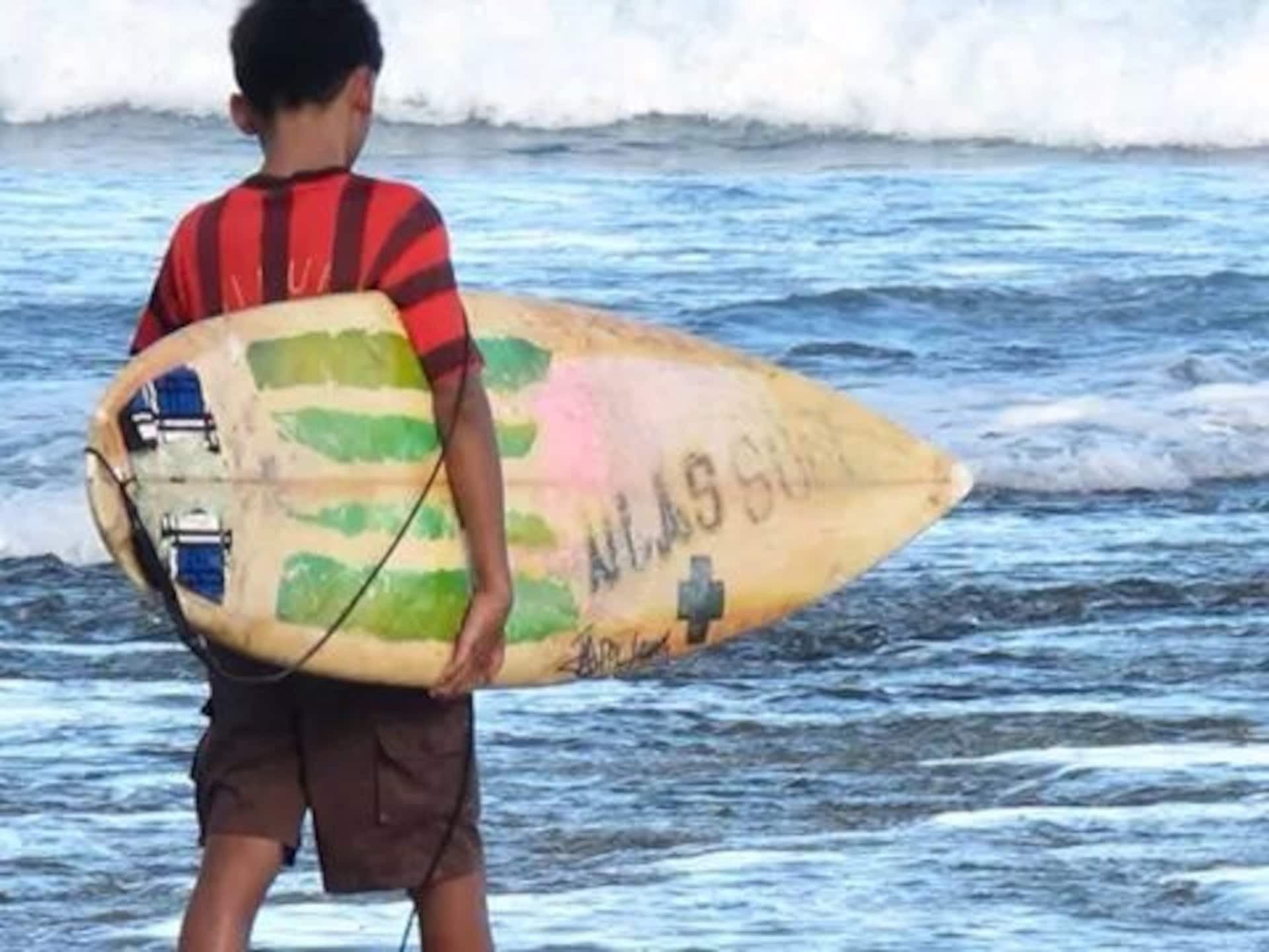 Young surfer carrying his board into the waves