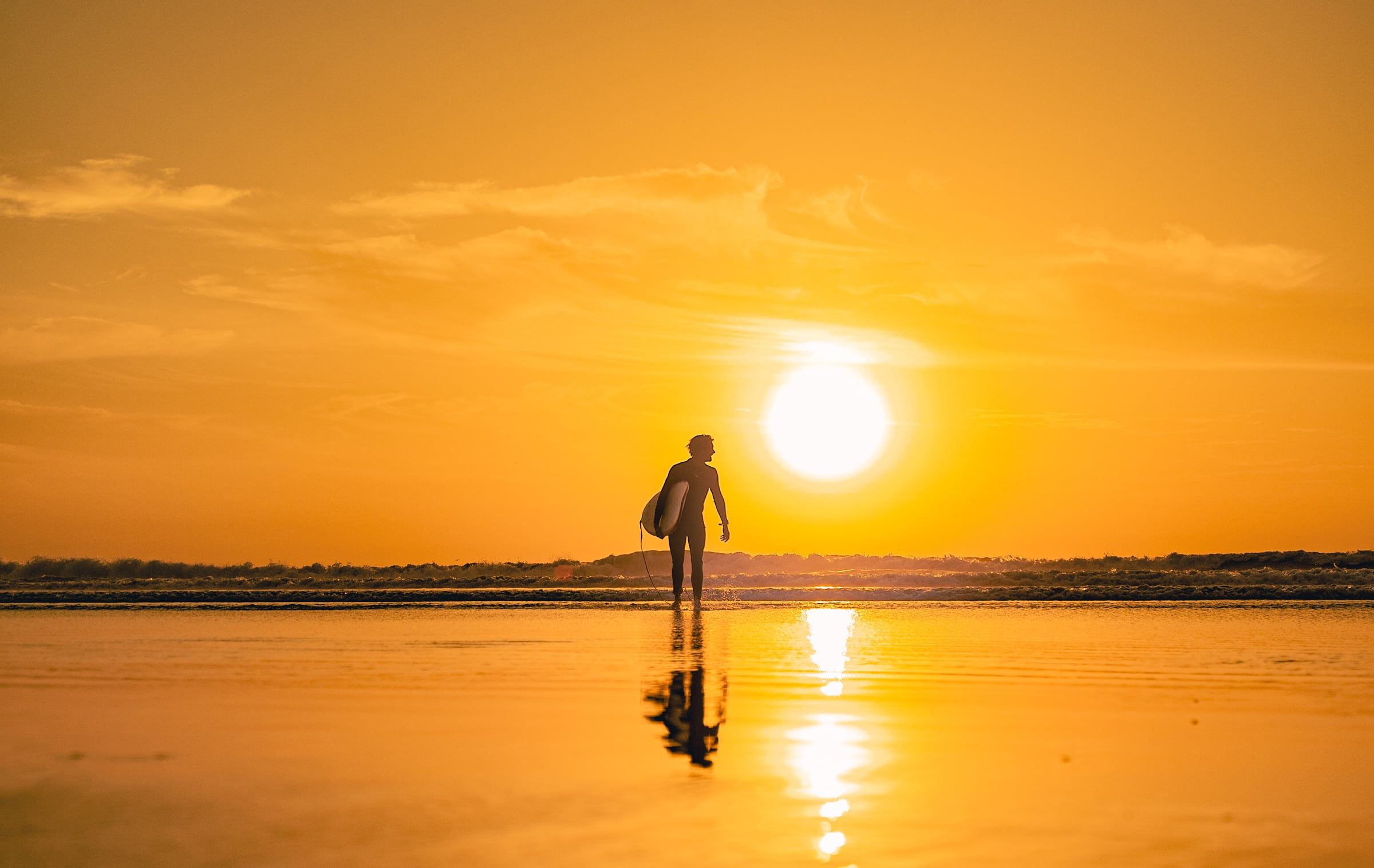 A surfer walking out of the water at sunset