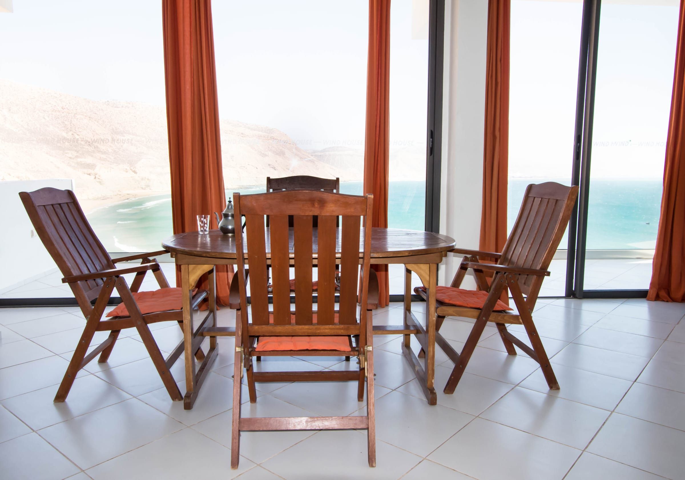 Dining table in front of the bay, framed by orange curtains