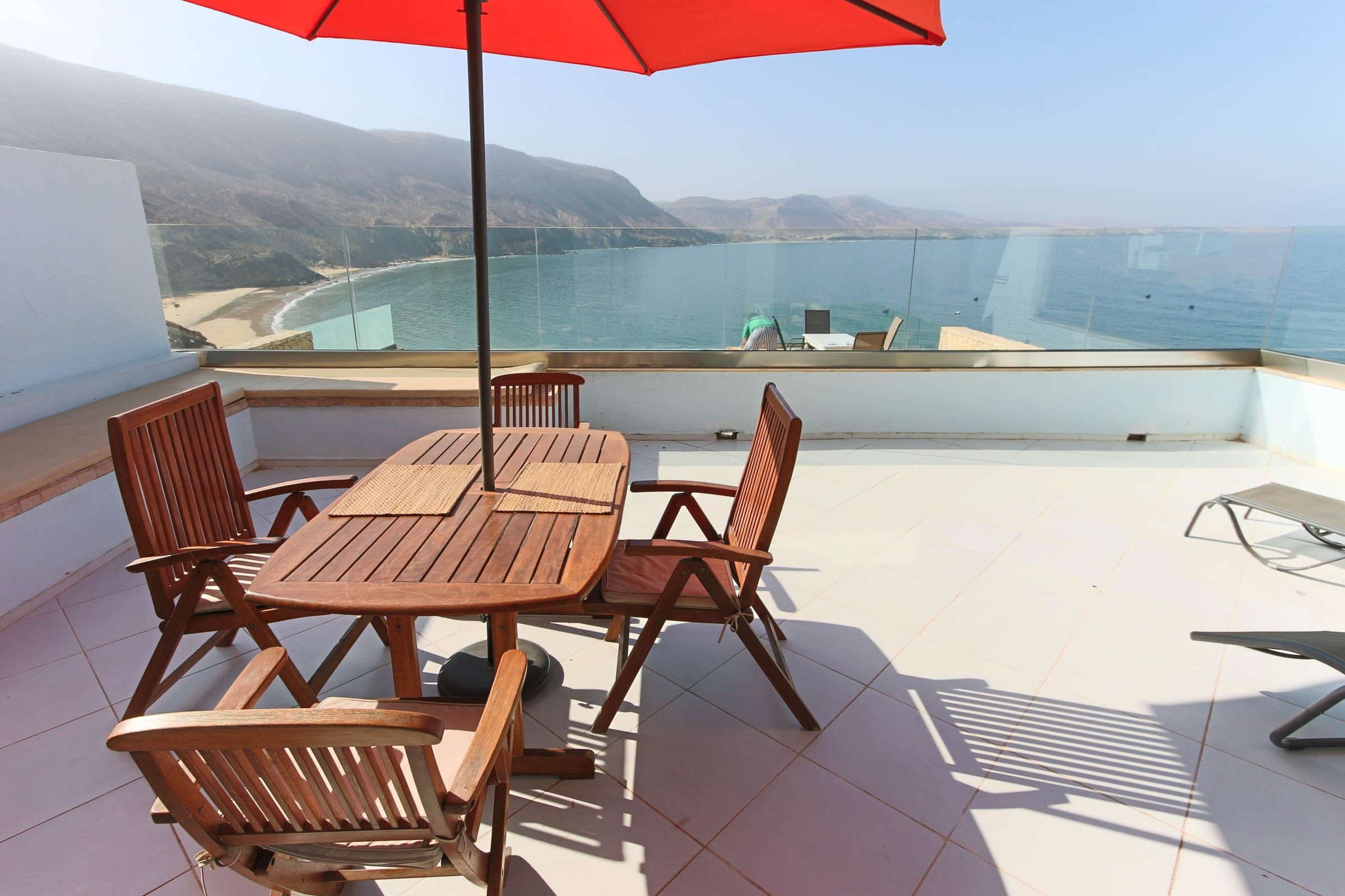 Terrace table under a red parasol, the bay behind